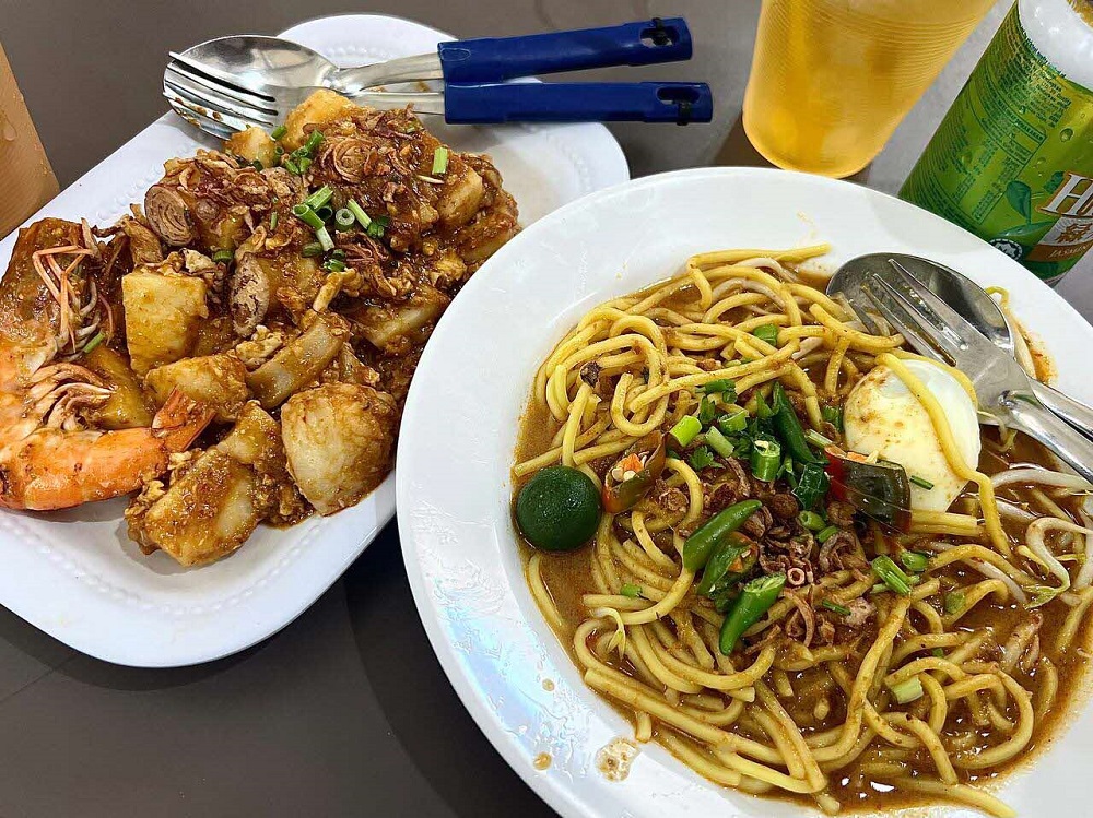 On Noraida’s recommendation, the authors sat down to a hearty meal of lontong goreng and mee rebus, the stall’s bestsellers. 2025. Photo courtesy of Afiqah Khalid.