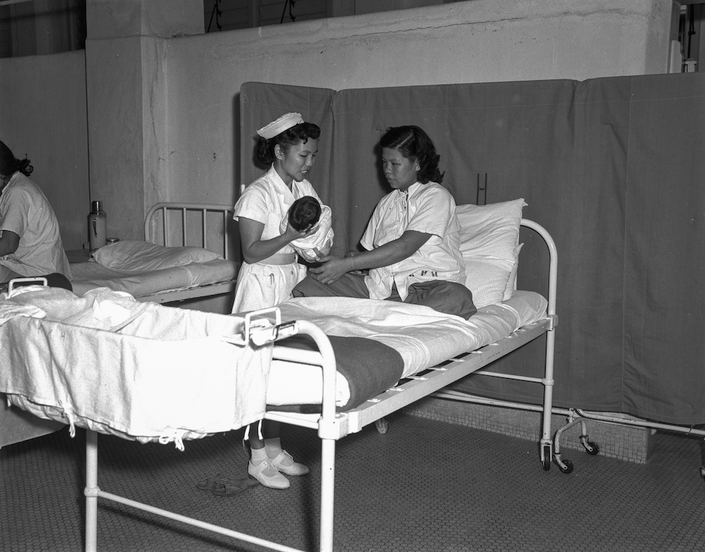 Nurse presenting a newborn baby to mother at the former KK Hospital, 19 March 1958. Courtesy of the National Archives of Singapore.