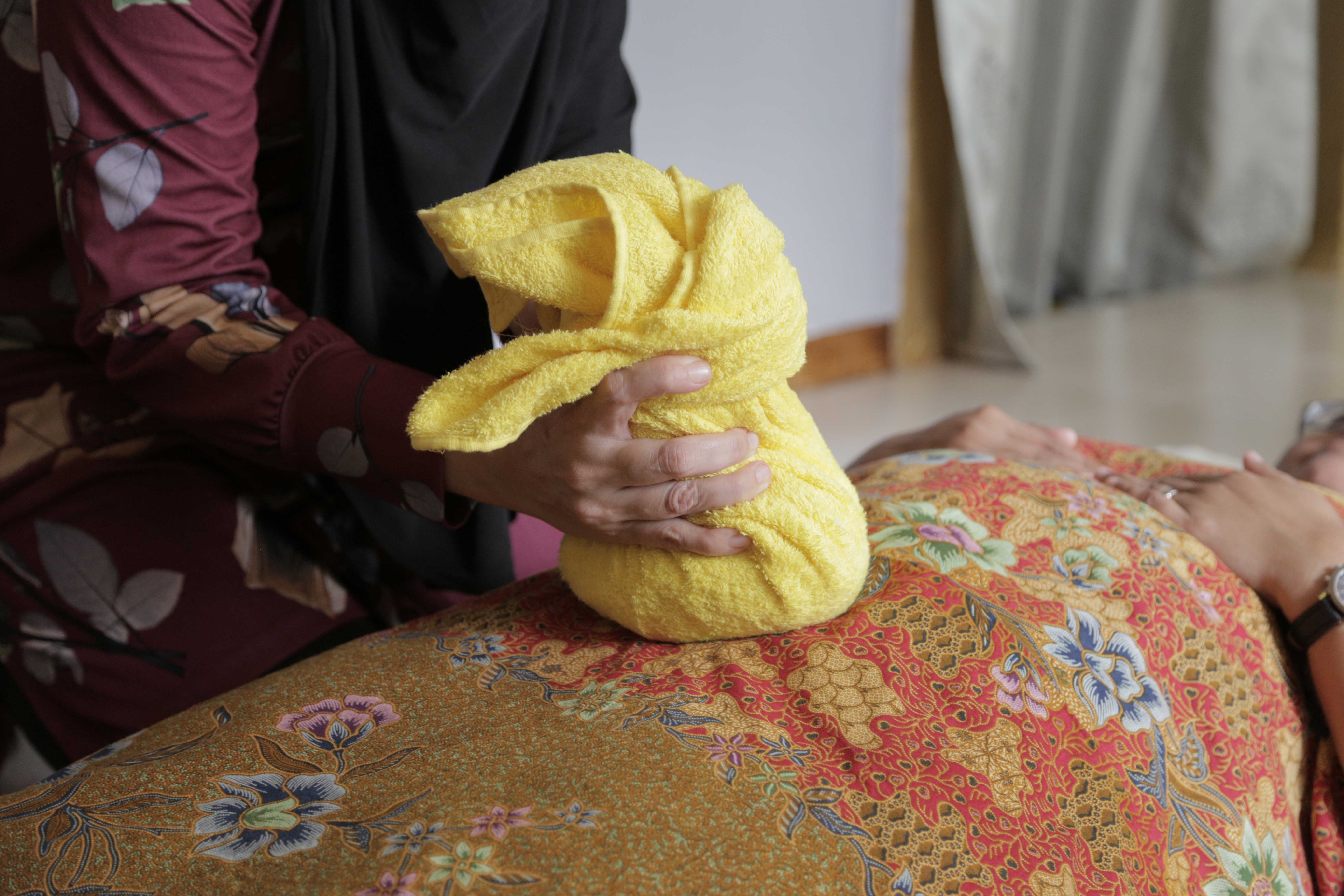 As part of birthing traditions practised by the Malay community, heated stone is placed on piled herbs, then wrapped with a towel for pressing on the woman’s abdomen. This process is called <i>tungku</i>.