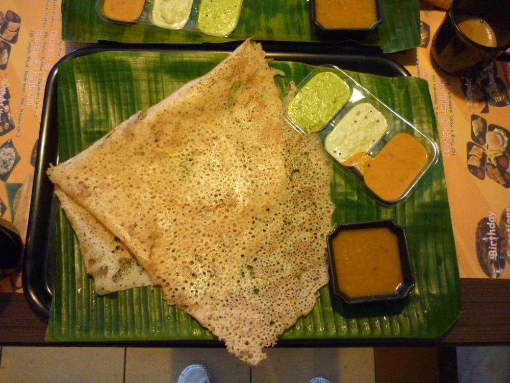 A rawa thosai, a thin pancake made from semolina and rice flour, served with three types of chutneys and a curry. A banana leaf, the traditional way of serving food in South India, is placed on the plate here. 