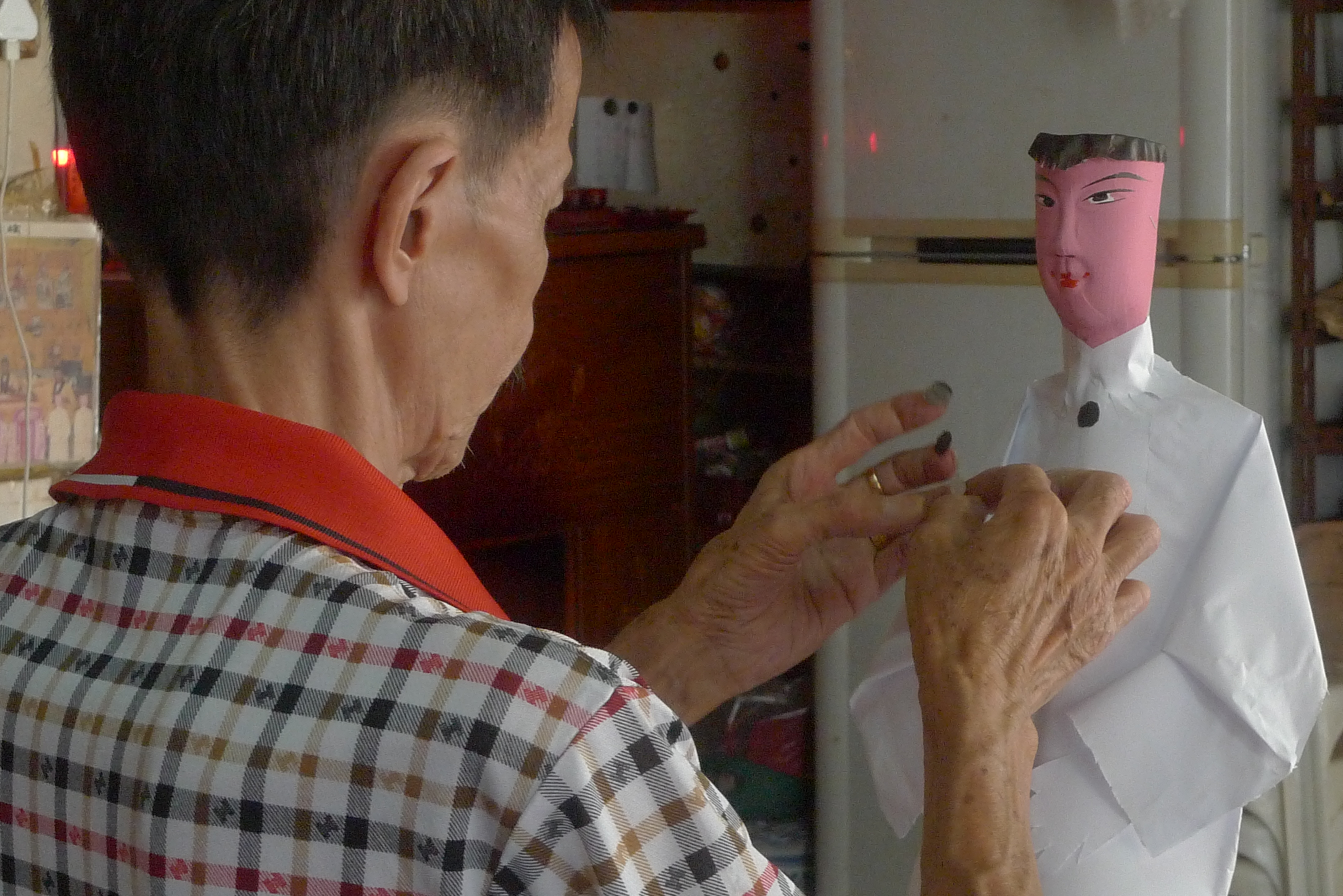 Mr Lai Yew Onn, the owner of Yew Chye Religious Goods Trading, creating the clothes of a paper human figure. 