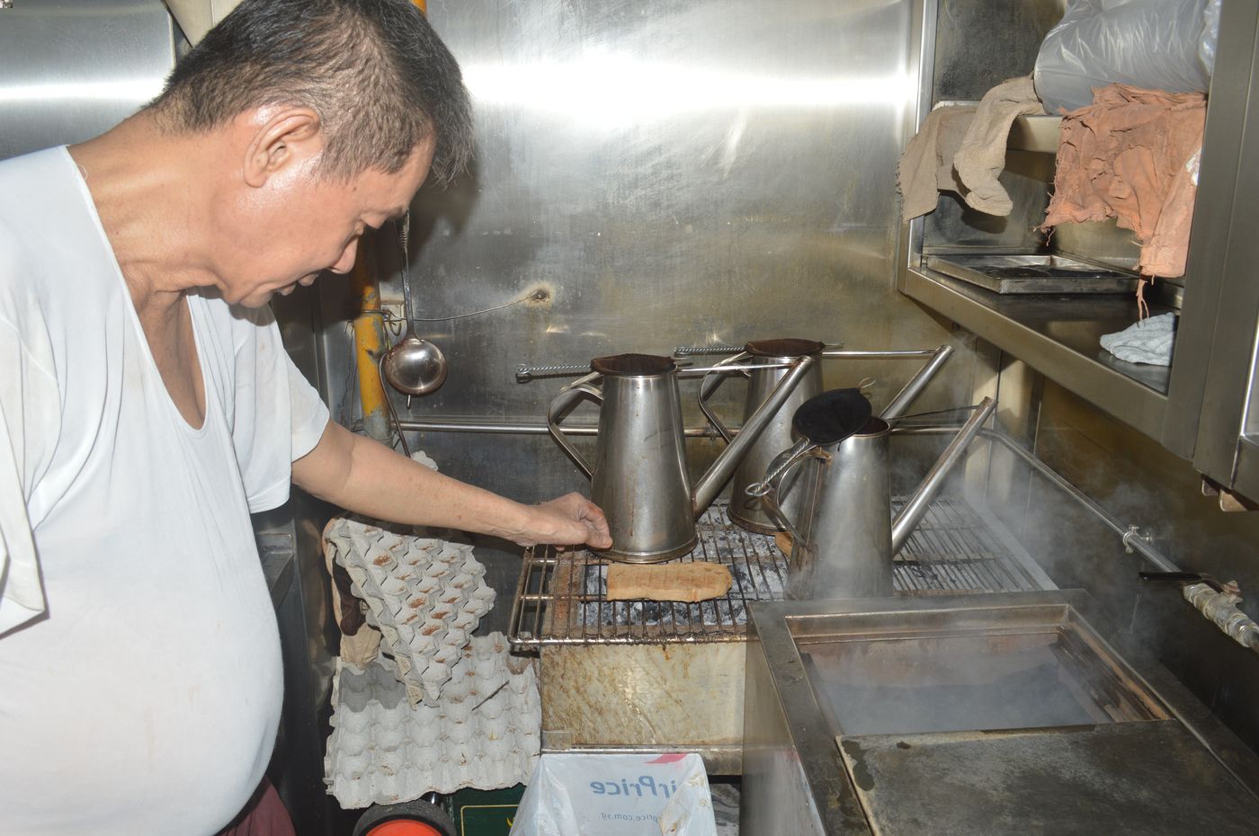 Mr Wong Lu Shen, owner of Ah Seng (Hai Nam) Coffee, toasting bread over charcoal embers at his stall.