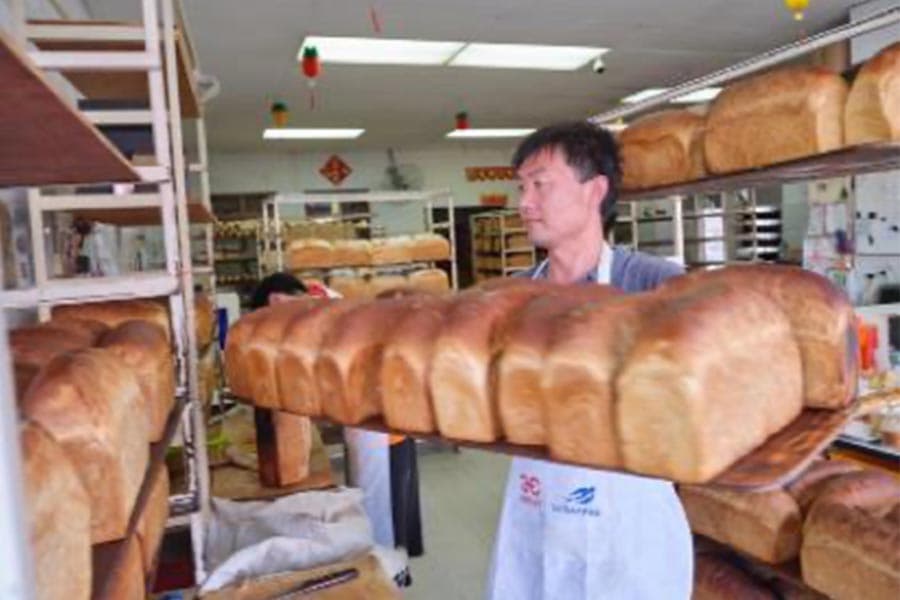 After baking, the loaves are taken out of the bread pans and allowed to cool down on wooden shelves before the bakers slice off the crust.&nbsp;