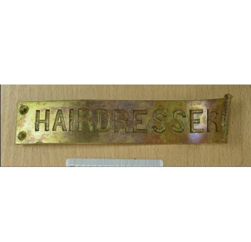 <em>Four brass signs revealing names of rooms generally associated with port side spaces were recovered. The Hairdresser was located on the port side Bridge Deck near the stern.</em>