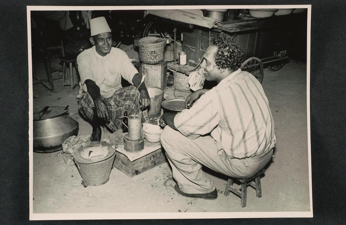 <strong>Malay hawker with customer<br>
</strong>c1950<br>
XXXX-15572