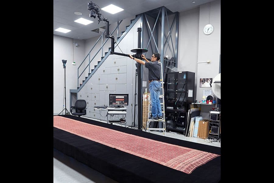 Dave is photographing a piece of textile (<a href="/collection-landing/listing/1232401">2009-02101</a>) which is about 5m long. Due to its length, it has to be taken with this setup. Dave ensures that the lighting is even across the entire textile.