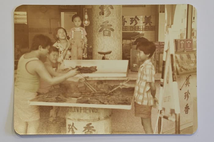 <span>Gambar ini, yang diambil pada tahun 1970-an, menunjukkan pekerja sedang barbeku bak kwa di cawangan New Bridge Road, dengan pemilik generasi ketiga sekarang ini dan ibunya di tengah-tengah.</span>