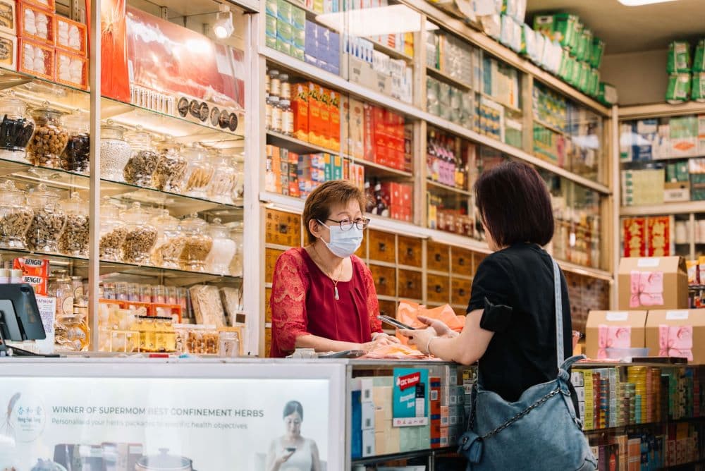 Mdm Chye Nyuk Lian serving a customer from the storefront of Heng Foh Tong Medical Hall.