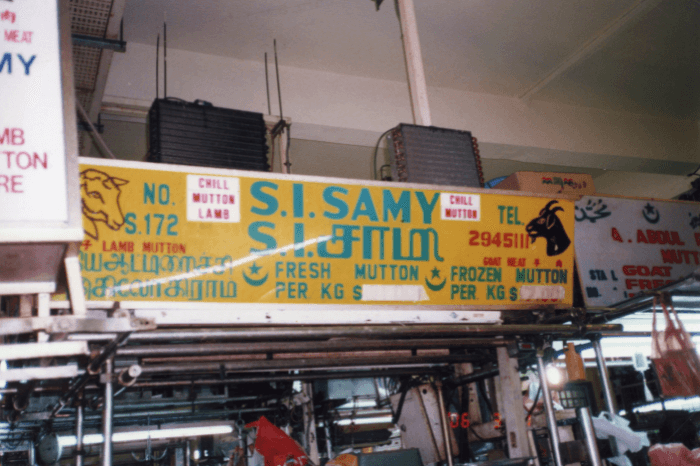 1970களில் எடுக்கப்பட்ட இந்தப் புகைப்படம், தேக்கா நிலையத்தில் இருந்த கடையின் பழைய பெயர்ப்பலகையைக் காட்டுகிறது. அதில் கடை நிறுவனரின் பெயர் தமிழிலும் ஆங்கிலத்திலும் இடம்பெற்றுள்ளது.
