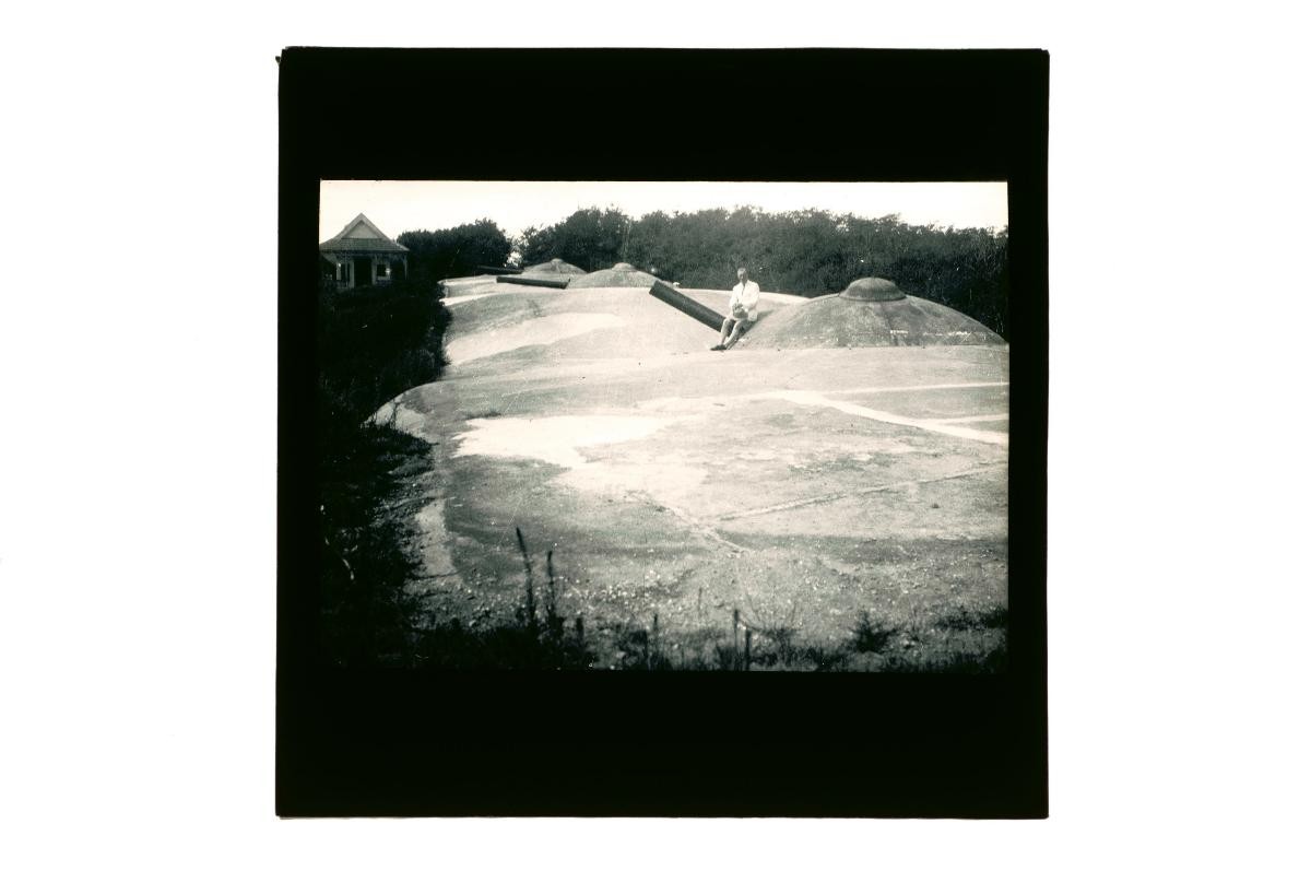 A glass lantern slide depicting a European man posing on a tank barrel