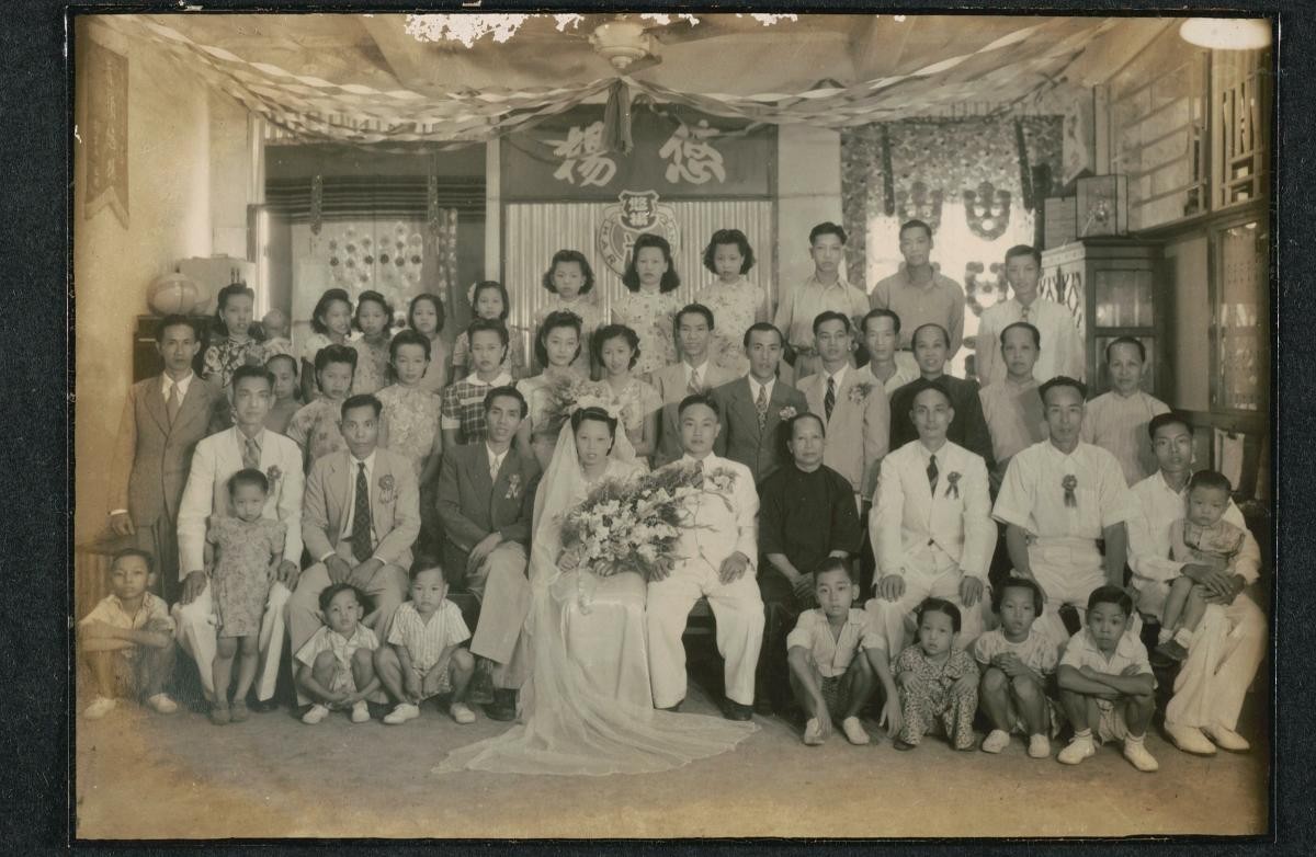 A Chinese bride and groom in Western wedding attire, with family and friends