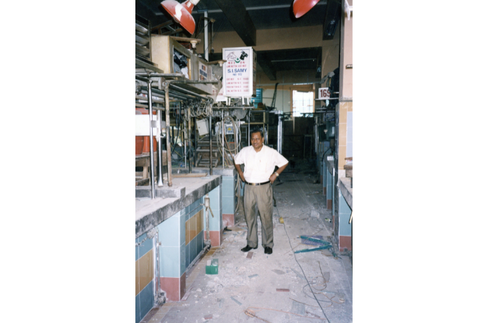Gambar ini menunjukkan Sinnasamy Irudayasamy berdiri di hadapan gerainya di pasar di Pusat Tekka yang baru dibina pada tahun 1982.