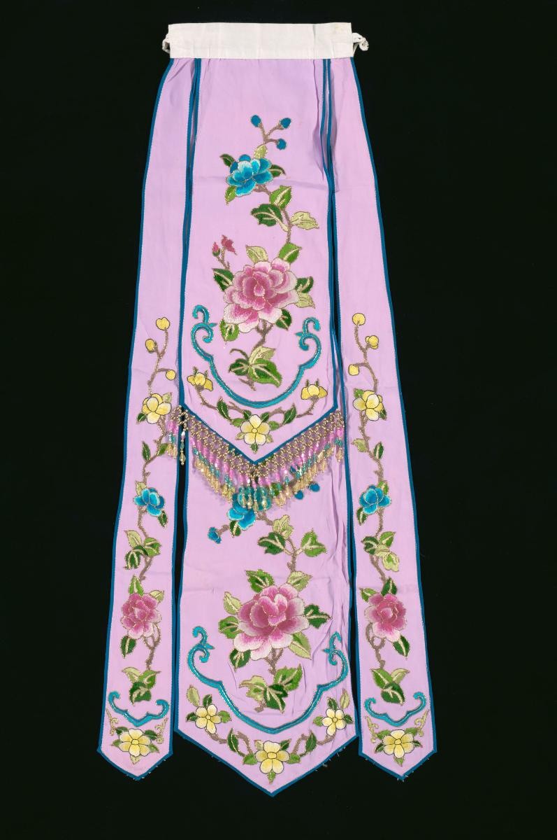 A pink waist piece with floral embroidery worn by a ‘hua dan’ in a Chinese opera