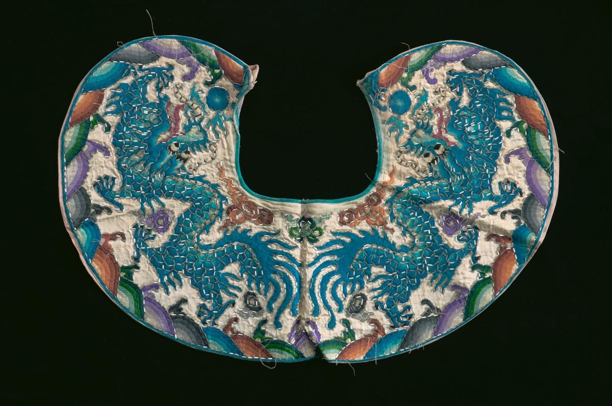 A white shoulder piece embroidered with blue dragon motifs worn by a court official in a Chinese opera