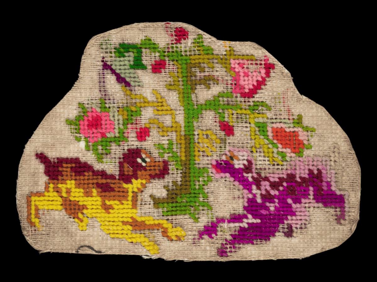 Needlework sampler with motifs of two dogs playing under a flowering plant