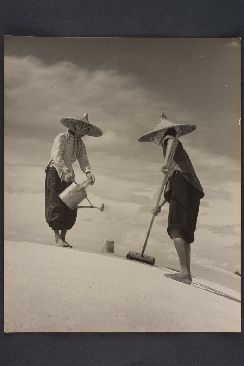Photograph of two workers with a watering can and a broom