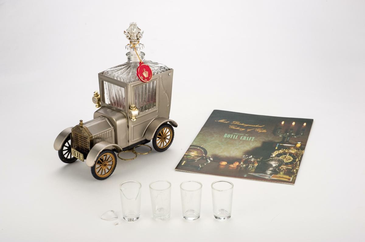 A bottle of wine with four small glasses housed in a mini car and a gift catalogue